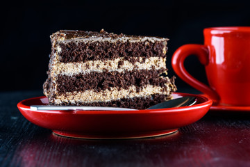a piece of chocolate cake on a plate next to a cup of coffee, on a dark wooden background. Homemade baking.Close-up view.