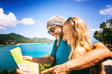 A young couple of travelers look in the map, sea and a beautiful tropical landscape. Travel, vacation, honeymoon concept