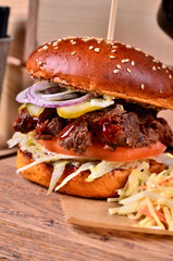 Fresh homemade hamburger with beef, onion, sause and cabbage garnish on a wooden board, wooden table background. Juicey gourmet burger, fast food concept.