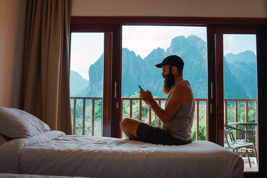 Side view of man using smartphone while sitting on bed