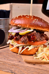 Fresh homemade hamburger with beef, onion, sause and cabbage garnish on a wooden board, wooden table background. Juicey gourmet burger, fast food concept. Text place, copy space