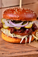 Fresh homemade hamburger with beef, onion, sause and cabbage garnish on a wooden board, wooden table background. Juicey gourmet burger, fast food concept.