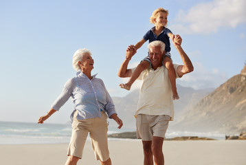 Grandparents Carrying Grandson On Shoulders On Walk Along Beach