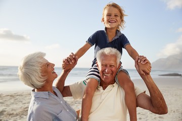 Grandparents Carrying Grandson On Shoulders On Walk Along Beach