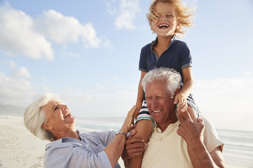 Grandparents Carrying Grandson On Shoulders On Walk Along Beach