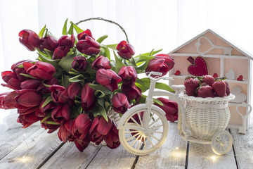 on the table in a basket there are a lot of red tulips and a basket with strawberries, lights 