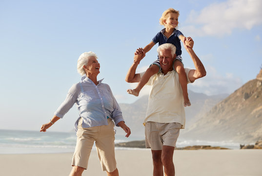 Grandparents Carrying Grandson On Shoulders On Walk Along Beach