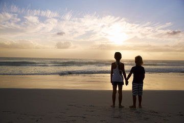 Fototapeta premium Rear View Of Children Holding Hands Silhouetted On Beach