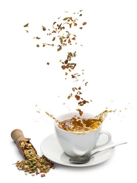 cup of tea with tea mixture falling and splashing on white background