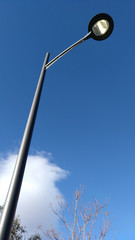 Farola de color negro encendida de día con cielo azul