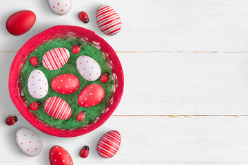 Colored eggs in baskets and on a white wooden table with empty space for adding text.