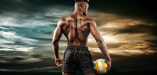 Portrait of afro-american sportsman, volleyball player with a ball over sky sunset. Fit young man in sportswear holding ball.