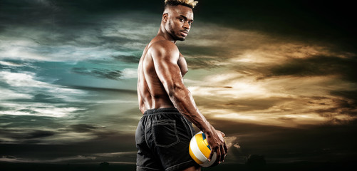 Portrait of afro-american sportsman, volleyball player with a ball over sky sunset. Fit young man in sportswear holding ball.