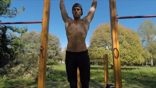 Attractive shirtless muscular young man exercising and working out in outdoor gym in city park