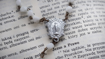 Miraculous Medal Holy Mother`s on open polish Holy Bible. Virgin Mary, medallion, rosary and Bible.
