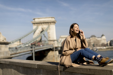 Fototapeta premium Young woman using mobile phone with Chain bridge at background in Budapest