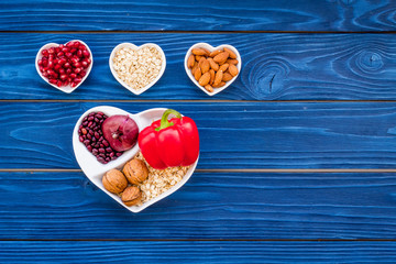 Food which help heart stay healthy. Vegetables, fruits, nuts in heart shaped bowl on blue wooden...