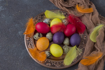 Easter composition: in the bronze plate lie red eggs, yellow eggs, violet eggs, quail eggs and feathers
