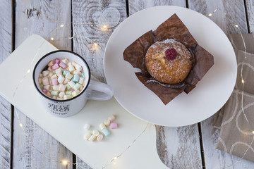 on the table a mug with cocoa and marshmallow, a muffin and a garland