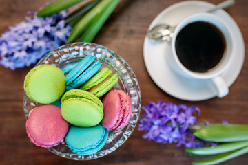 A cup of coffee and a vase with macaroons, flowers of hyacinths on a wooden table. Top view, selective focus.