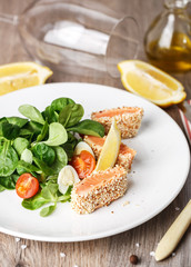 salad with salmon grilled in sesame seeds, cherry tomatoes and quail egg on wooden table