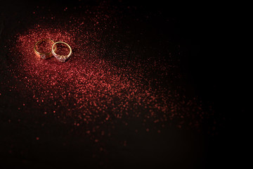 Gold wedding rings with red glitter and red bokeh on black background.