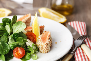 salad with salmon grilled in sesame seeds, cherry tomatoes and quail egg on wooden table