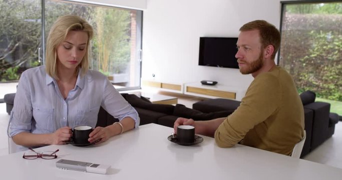 Attractive couple having awkward coffee, not speaking to each other in contemporary house,