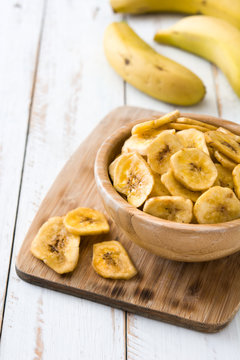 Banana chips in bowl on white wooden table.
