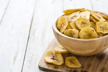 Banana chips in bowl on white wooden table. Copyspace