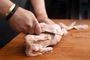 Male hands prepare a raw chicken with a kitchen knife for cooking on a rustic wooden butcher block