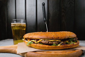 Big burger and beer on a wooden stand.