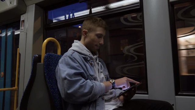 A happy young man using a digital tablet while commuting in a tram. Three quarter length. Side view. Profile.