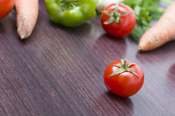 Red tomatoes and green peppers on a table on the background of vegetables. Fresh tomatoes and peppers on a wooden brown table..