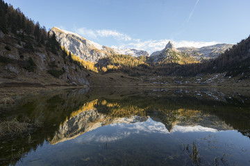 Herbstliche Bergwälder und schneebdeckte Berggipfel in der Abendsonne spiegeln sich im stillen Funtensee in den Bergen des Nationalpark Berchtesgaden, Bayern, Deutschland