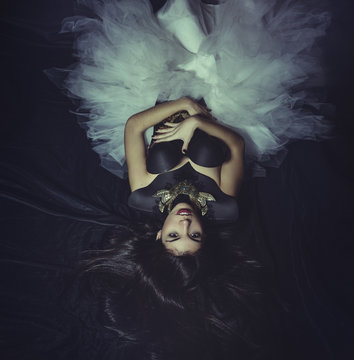 black swan, brunette woman on the floor covered in black fabrics and jewelry corset with white tutu