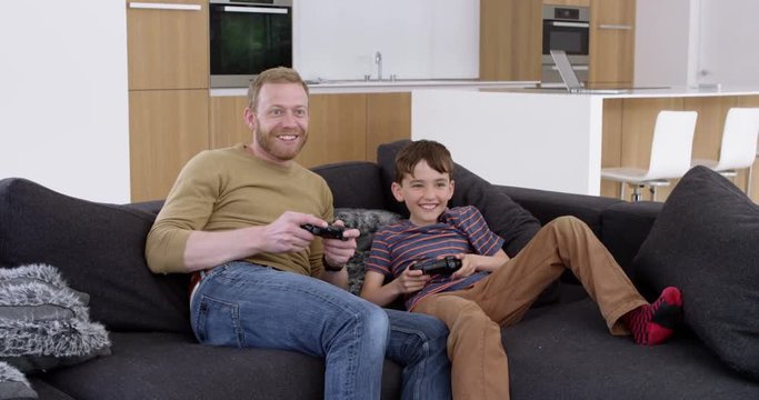 Father and son both jump onto sofa to play games console in beautiful contemporary home,