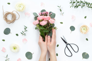 Small bouquet of pink bush roses in a woman's hand on a white background, top view, flat lay, copy...