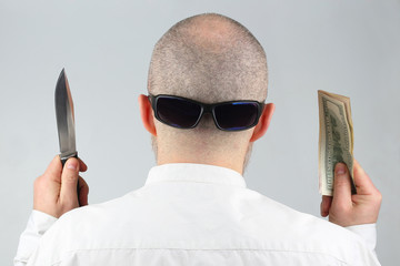 man stands with his back with money and a knife in his hands.