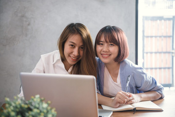 Two young business women sitting at table in cafe. Asian women using laptop and cup of coffee. Freelancer working in coffee shop. Working outside office lifestyle. One-on-one meeting.