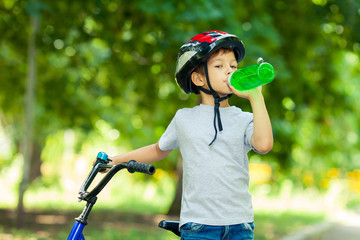 Little boy drinking water by the bike. Child in helmet riding a cycling.