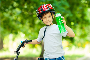 Little boy drinking water by the bike. Happy smiling child in helmet riding a cycling.