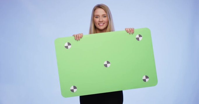 Beautiful young Lady is lifting up an oversized blank Card and giving a stunning smile to the Camera