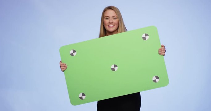 Cheerful young Woman coming  into the picture holding an oversized greenscreen Card and then leaving picture