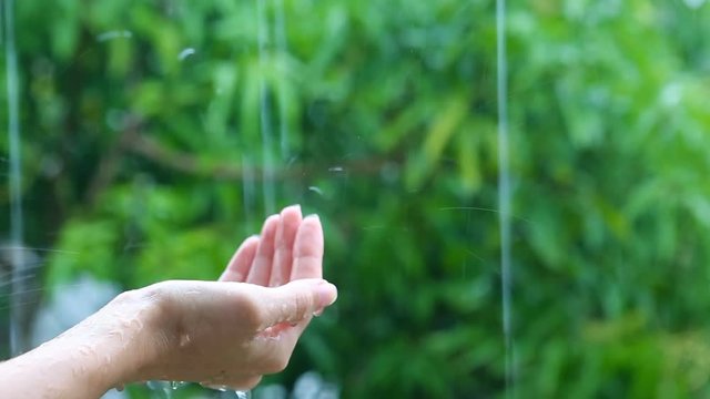 Hand under the rain, rainwater close-up. Woman putting her hand out to feel raindrops on her palm.