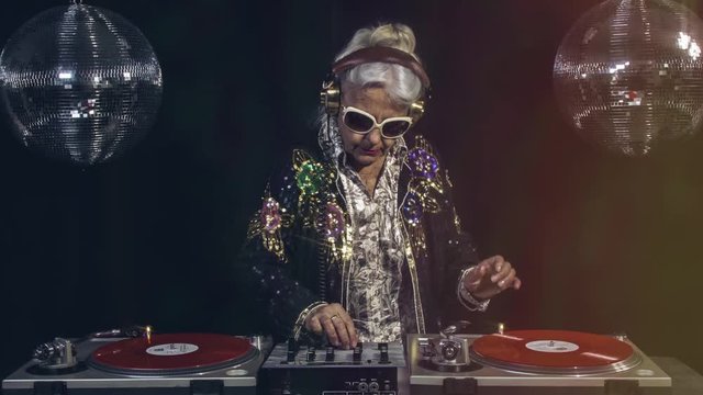 amazing DJ grandma scratching vinyl, older lady djing and partying in a disco setting. these retired rockers will get the party going.