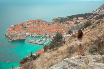 Obraz premium Brunette Girl tourist visiting mountain viewpoint sightseeing in Dubrovnik, Croatia. Woman traveller in front on famous travel destination. Free brunette enjoying vacation.