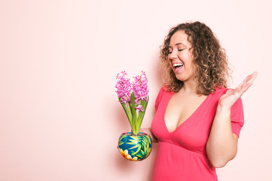 Beautiful curly woman surprised in red dress with hyacinth flowers in hands on a light pink background. Hello spring concept.