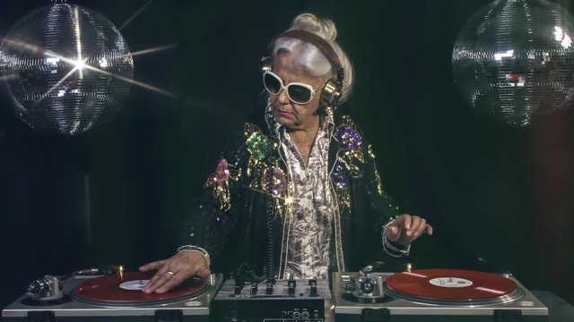 amazing DJ grandma scratching vinyl, older lady djing and partying in a disco setting. these retired rockers will get the party going.