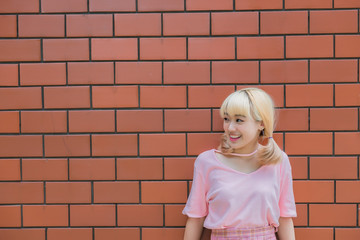 Portrait of thai woman golden hairs japan style on orange brick wall,Asian girl pose for take a picture outdoor